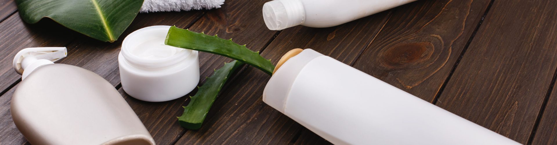 White towel, bottles of shampoo and conditioner lie on a table with green leaf and aloe